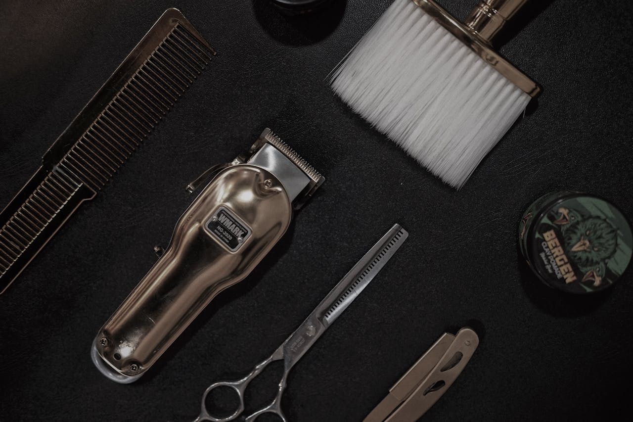 why-choose-us Flat lay of barber tools including clipper, scissors, and comb on a black surface.